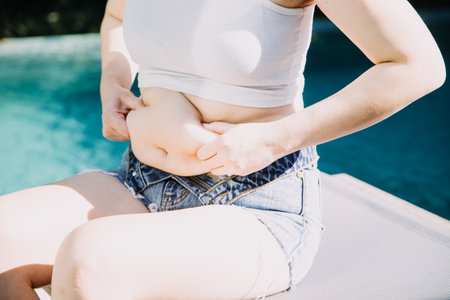 fat woman, fat belly, chubby, obese woman hand holding excessive belly fat with measure tape, woman diet lifestyle conceptの写真素材