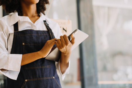 Startup successful small business owner sme beauty girl stand with tablet smartphone in coffee shop restaurant. Portrait of asian tan woman barista cafe owner. SME entrepreneur seller business conceptの写真素材