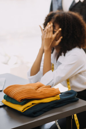 Female fashion, designer, Looking at Drawings and Sketches that are Pinned to the Wall Behind Her Desk. Studio is Sunny. Personal Computer, Colorful Fabrics, Sewing Items are Visible.の写真素材