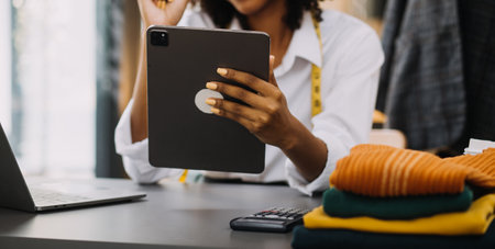 Female fashion, designer, Looking at Drawings and Sketches that are Pinned to the Wall Behind Her Desk. Studio is Sunny. Personal Computer, Colorful Fabrics, Sewing Items are Visible.の写真素材