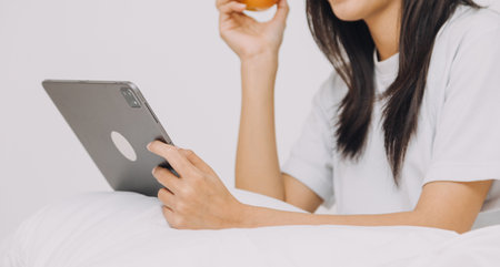 Female students note from the books at the Asian girl library sitting at sofa using laptop computer and tablet to search an online informations. in living roomの写真素材