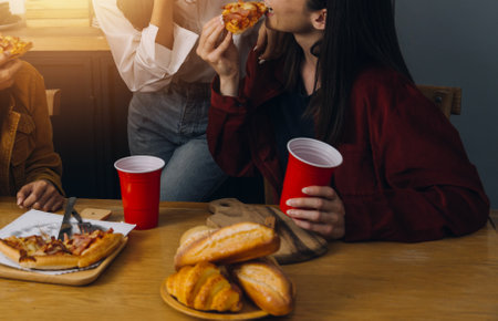 Friends hangout. Young female celebrating birthday party at weekend at home, eating pizza, drinking champagne, party, lifestyle, friendshipの写真素材