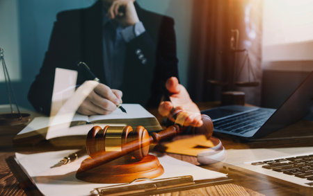Justice and law concept.Male judge in a courtroom with the gavel, working with, computer and docking keyboard, eyeglasses, on table in morning lightの写真素材