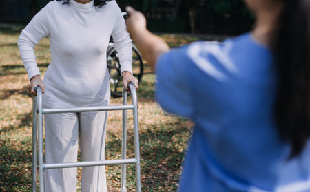 Asian young woman nurse at nursing home take care disabled senior man. Caregiver doctor serve physical therapy for older elderly patient to exercise and practice walking on walker or cane at backyard.の写真素材
