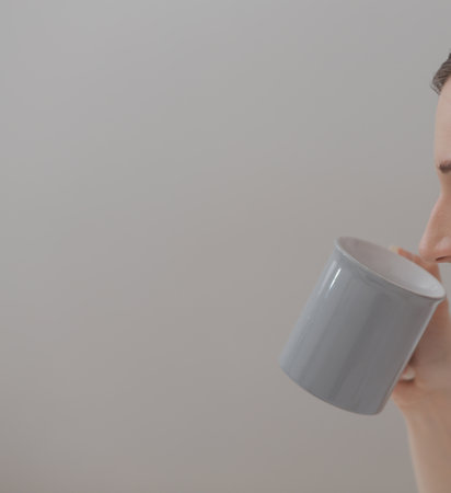 Efficient Young Millennial Girl Sitting on a Bed in the Morning, Uses Laptop Computer and Eats Croissants and Drinks Coffee for Breakfastの写真素材