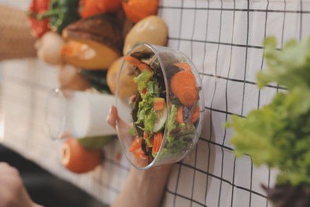 Delicious fruit and vegetables on a table and woman cooking. Housewife is cutting green cucumbers on a wooden board for making fresh salad in the kitchen.の写真素材