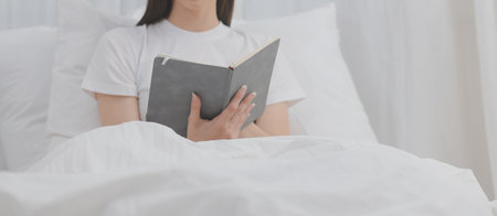 Efficient Young Millennial Girl Sitting on a Bed in the Morning, Uses Laptop Computer and Eats Croissants and Drinks Coffee for Breakfastの写真素材