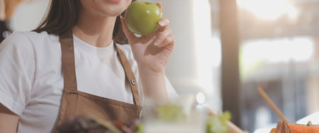 Delicious fruit and vegetables on a table and woman cooking. Housewife is cutting green cucumbers on a wooden board for making fresh salad in the kitchen.の写真素材