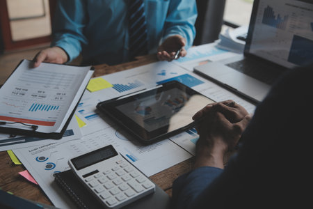 Financial analysts analyze business financial reports on a digital tablet planning investment project during a discussion at a meeting of corporate showing the results of their successful teamwork.の写真素材