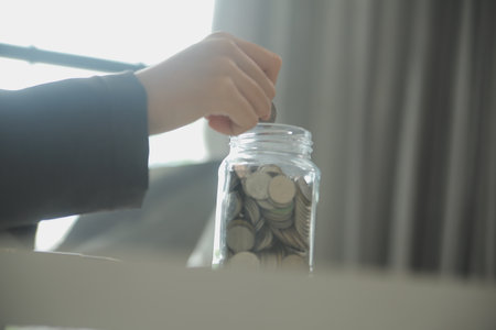 saving money and accounting concept. business man putting coin insert to jar and make acounting book for finance management to investment and saving.の写真素材