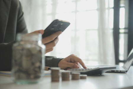 saving money and accounting concept. business man putting coin insert to jar and make acounting book for finance management to investment and saving.の写真素材