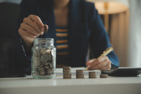 saving money and accounting concept. business man putting coin insert to jar and make acounting book for finance management to investment and saving.の写真素材