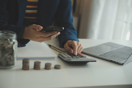saving money and accounting concept. business man putting coin insert to jar and make acounting book for finance management to investment and saving.の写真素材