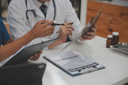 Focused mature male doctor and female nurse look at tablet screen discuss anamnesis together. Concentrated diverse medical professionals use pad device, engaged in team thinking in hospital.の写真素材