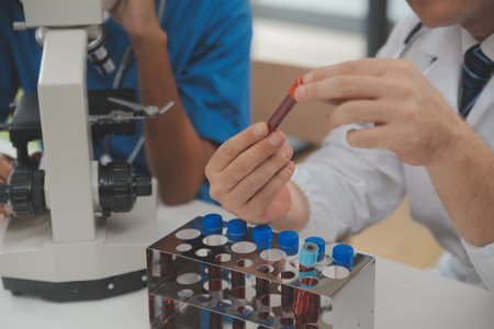 Medical worker in lab coat and sterile mask, doing a microscope analysis while her colleague are...