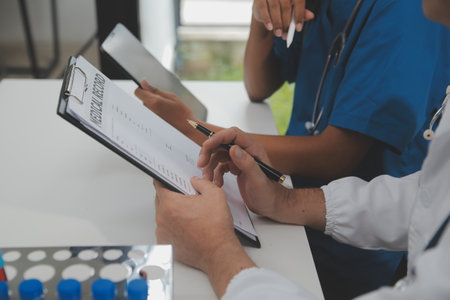 Medical worker in lab coat and sterile mask, doing a microscope analysis while her colleague are working behindの写真素材