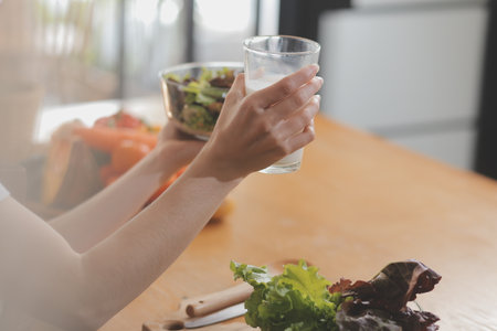 Delicious fruit and vegetables on a table and woman cooking. Housewife is cutting green cucumbers on a wooden board for making fresh salad in the kitchen.の写真素材