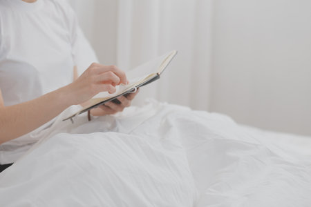 Efficient Young Millennial Girl Sitting on a Bed in the Morning, Uses Laptop Computer and Eats Croissants and Drinks Coffee for Breakfastの写真素材