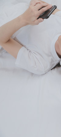 Efficient Young Millennial Girl Sitting on a Bed in the Morning, Uses Laptop Computer and Eats Croissants and Drinks Coffee for Breakfastの写真素材