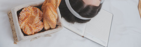 Efficient Young Millennial Girl Sitting on a Bed in the Morning, Uses Laptop Computer and Eats Croissants and Drinks Coffee for Breakfastの写真素材