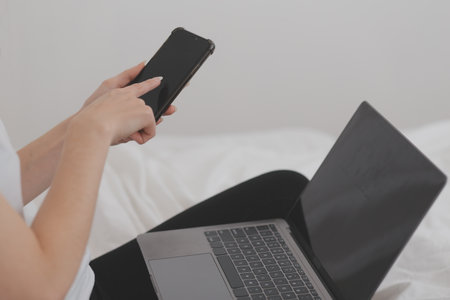 Efficient Young Millennial Girl Sitting on a Bed in the Morning, Uses Laptop Computer and Eats...