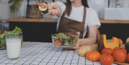 Delicious fruit and vegetables on a table and woman cooking. Housewife is cutting green cucumbers on a wooden board for making fresh salad in the kitchen.の写真素材