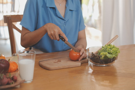A young woman with a beautiful face in a blue shirt with long hair eating fruit sitting inside the kitchen at home with a laptop and notebook for relaxation, Concept Vacation.の写真素材