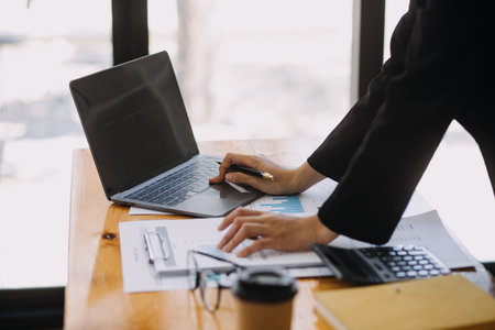 Asian Businesswoman Using laptop computer and working at office with calculator document on desk, doing planning analyzing the financial report, business plan investment, finance analysis concept.の写真素材