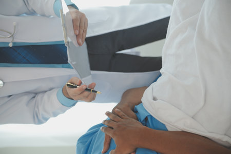 Close up of doctor sitting on bedside of male patient in hospitalの写真素材