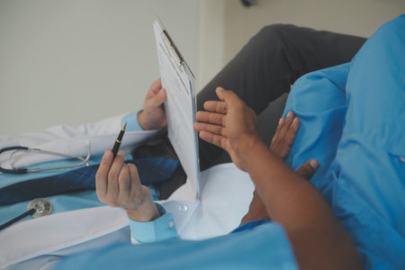 Close up of doctor sitting on bedside of male patient in hospitalの写真素材