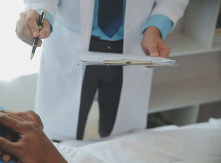 Close up of doctor sitting on bedside of male patient in hospitalの写真素材