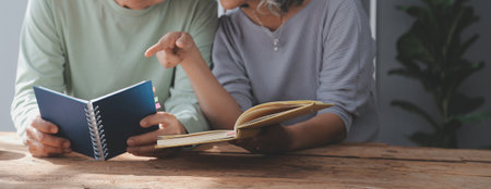 senior asian couple sitting on couch reading a book togetherの写真素材