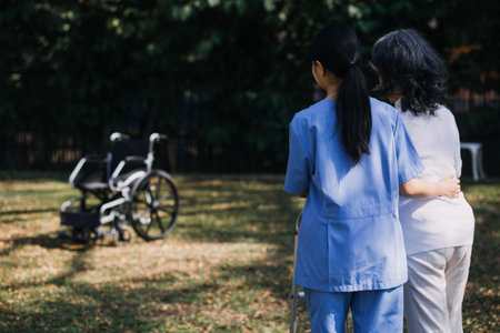 Asian young woman nurse at nursing home take care disabled senior man. Caregiver doctor serve physical therapy for older elderly patient to exercise and practice walking on walker or cane at backyard.の写真素材