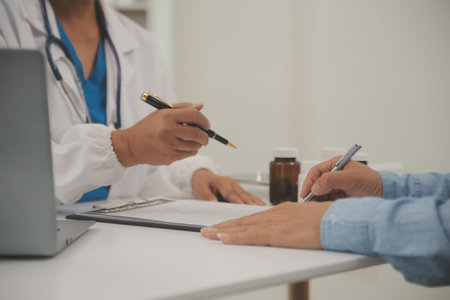 Doctor and patient sitting and talking at medical examination at hospital office, close-up. Therapist filling up medication history records. Medicine and healthcare concept.の写真素材