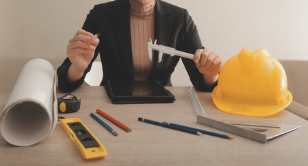 asian woman architect in shirt looking on internet online blueprint document project of green building. female interior designer worker working desktop computer monitor typing keyboardの写真素材