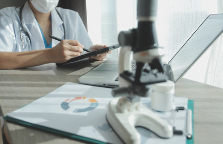 Young scientists conducting research investigations in a medical laboratory, a researcher in the foreground is using a microscopeの写真素材