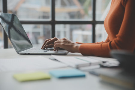 Asian Businesswoman Using laptop computer and working at office with calculator document on desk, doing planning analyzing the financial report, business plan investment, finance analysis concept.の写真素材