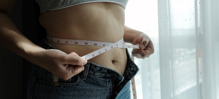 Close up of a belly with scar from c-section and abdominal fat. Women's health. A woman dressed up in sportswear demonstrating her imperfect body after a childbirth with nursery on the background.の写真素材
