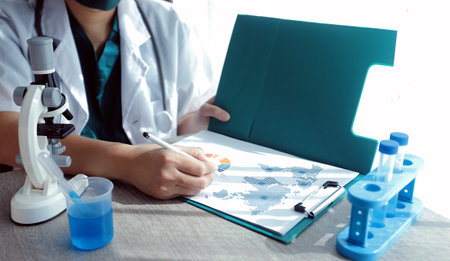 Research and experiments in the pharmaceutical or chemical industry. Female scientist in lab or chemist making notes on laptop by studying liquid in test tube. Scientists working on the background.の写真素材