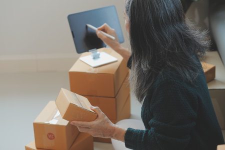 Startup SME small business entrepreneur of freelance Asian woman using a laptop with box Cheerful success Asian woman her hand lifts up online marketing packaging box and delivery SME idea conceptの写真素材