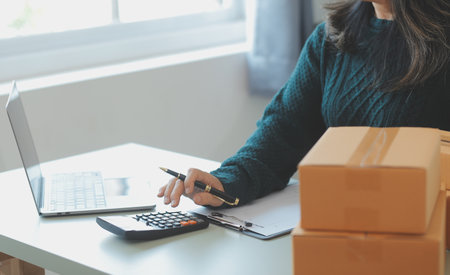 Startup SME small business entrepreneur of freelance Asian woman using a laptop with box Cheerful success Asian woman her hand lifts up online marketing packaging box and delivery SME idea conceptの写真素材