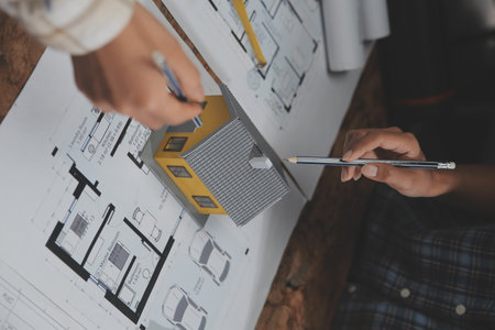 Team of multiethnic architects working on construction plans in meeting room. Engineers discussing on project in office. Mature businessman and woman standing around table working on blueprint.の写真素材