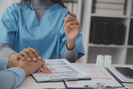 Young woman comes to clinic for heart and lungs checkup. Friendly female doctor sitting at desk in modern medical office, holding stethoscope, listening to patient's breath or heartbeat and smilingの写真素材