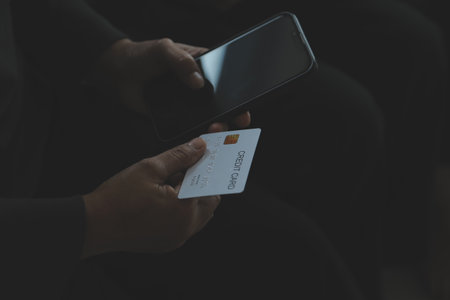 A credit card in the hands of a young businesswoman pays for a business on a mobile phone and on a desk with a laptop.の写真素材