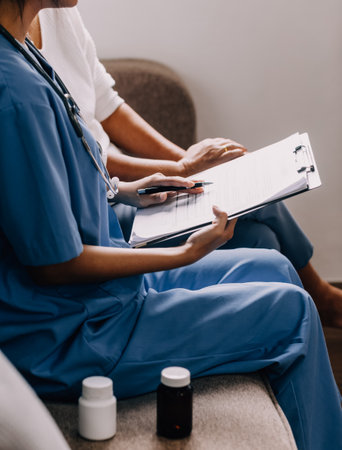 Caring doctor teaches female patient to use mobile healthcare app. Retired lady sitting in hospital...