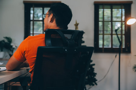 Satisfied caucasian successful guy, freelancer or ceo, relaxes at workplace with legs thrown on table. Stylish guy uses laptop, browses the Internet, looks for ideas for a project, sitting at the deskの写真素材