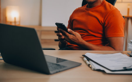Satisfied caucasian successful guy, freelancer or ceo, relaxes at workplace with legs thrown on table. Stylish guy uses laptop, browses the Internet, looks for ideas for a project, sitting at the deskの写真素材