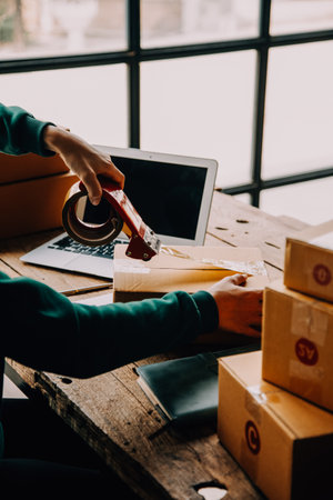 Startup small business entrepreneur or freelance Asian woman using a laptop with box, Young success Asian woman with her hand lift up, online marketing packaging box and delivery, SME concept.の写真素材