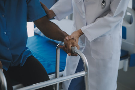 Rehabilitation of disabled people concept. Young physiotherapist helping senior male patient in wheelchair exercise at home. Handicapped elderly man training with dumbbellsの写真素材