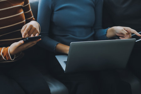 Three beautiful Asian girls using smartphone and laptop, chatting on sofa together at cafe with copy space, modern lifestyle with gadget technology or working woman on casual business conceptの写真素材